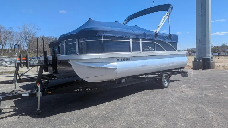 Slide: The Image of 2020 Bennington 20SLV pontoon boat on trailer with blue cover, parked outdoors. - 5