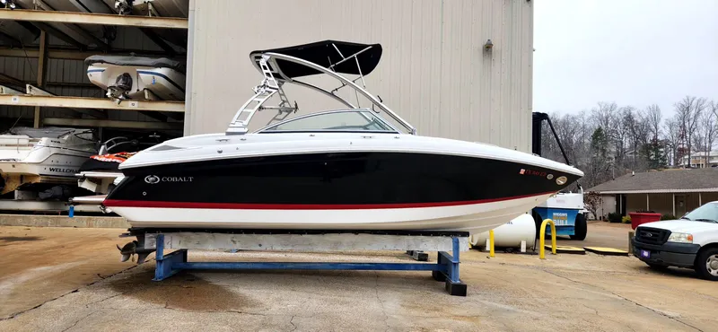 Slide: The Image of 2011 Cobalt 242 boat with black hull and red stripe, displayed on a stand outdoors. - 2