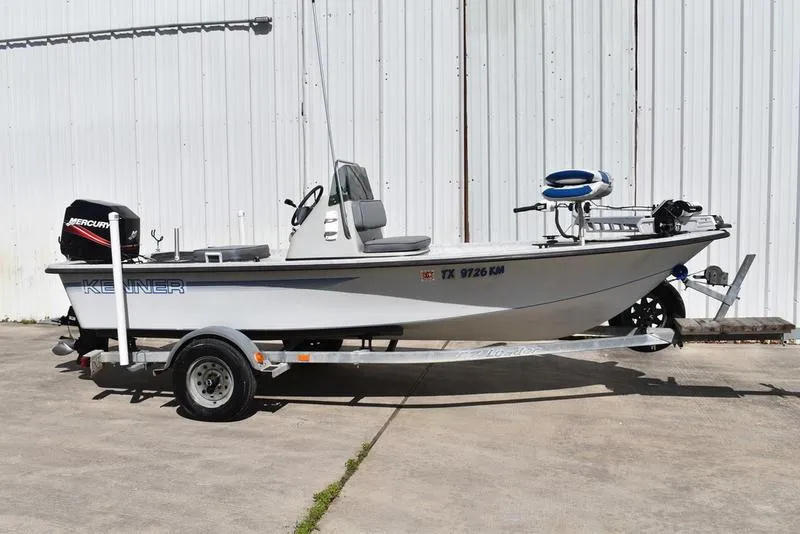 Slide: The Image of 1996 Kenner 16v boat on trailer, white hull, Mercury outboard motor, parked by a white wall. - 0