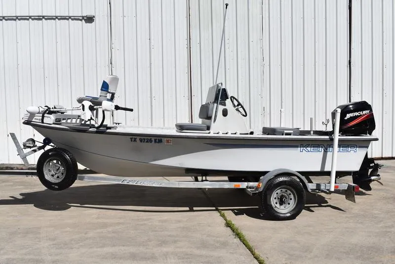 Slide: The Image of 1996 Kenner 16v boat on trailer, white exterior, Mercury outboard motor, parked by metal wall. - 2