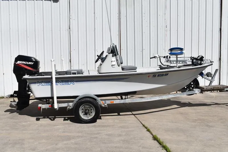 Slide: The Image of 1996 Kenner 16v boat on trailer with Mercury outboard motor, parked by a white wall. - 3