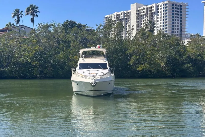 Slide: The Image of 2007 Azimut 55E yacht cruising on a calm river with lush greenery and buildings in the background. - 2