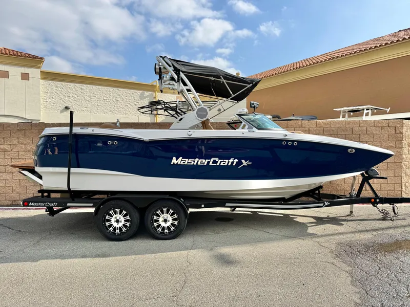 Slide: The Image of 2022 MasterCraft XStar boat on trailer, parked outdoors, blue and white design. - 0