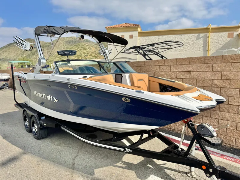 Slide: The Image of 2022 MasterCraft XStar boat on trailer, blue and white, parked outdoors. - 1