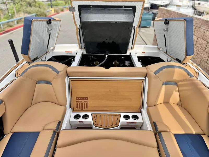 Slide: The Image of 2022 MasterCraft XStar boat interior with tan and blue seating, open storage compartments. - 21