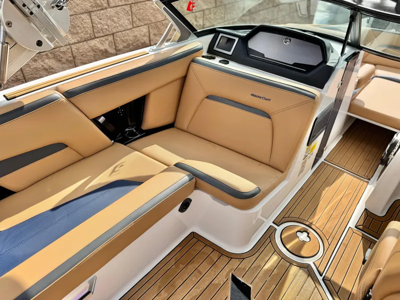 Slide: The Image of 2022 MasterCraft XStar boat interior with tan and black seating, wood flooring, and modern dashboard. - 28