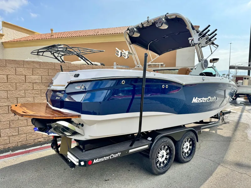 Slide: The Image of 2022 MasterCraft XStar boat on trailer, blue and white design, parked outdoors. - 5