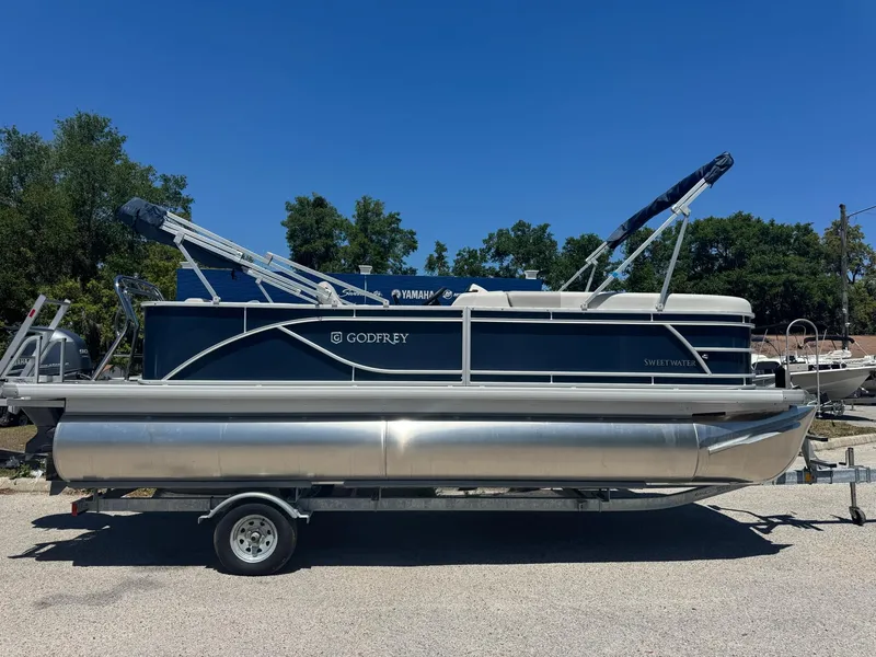 Slide: The Image of 2025 Sweetwater 2286 C pontoon boat on trailer, parked outdoors under clear blue sky. - 1