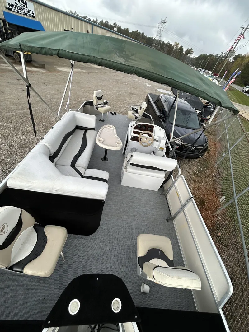 Slide: The Image of 2000 Fisher Freedom 200 DLX pontoon boat with canopy and seating, parked near a fence. - 5