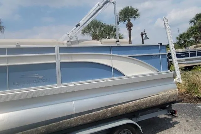 Slide: The Image of 2016 Bennington 21SFX pontoon boat on trailer, parked outdoors with palm trees. - 2