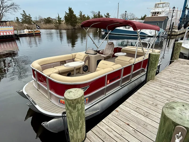 Slide: The Image of 2019 Bentley Pontoons 223 Elite docked, featuring red exterior and beige seating, under a canopy. - 1