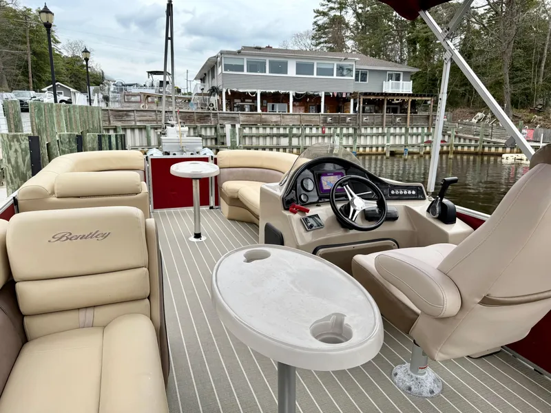 Slide: The Image of 2019 Bentley Pontoons 223 Elite interior with beige seating and modern dashboard, docked by a waterfront. - 13
