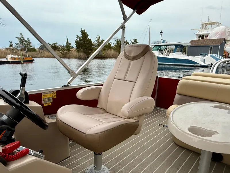 Slide: The Image of 2019 Bentley Pontoons 223 Elite interior with captain's chair and table on a calm waterway. - 16