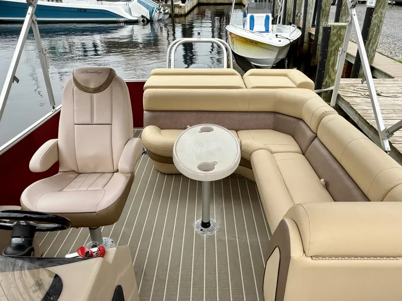 Slide: The Image of 2019 Bentley Pontoons 223 Elite interior with beige seating and table, docked by the water. - 17