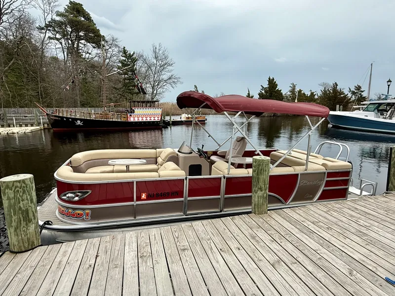 Slide: The Image of 2019 Bentley Pontoons 223 Elite docked, featuring red canopy and beige seating, in a serene marina setting. - 4