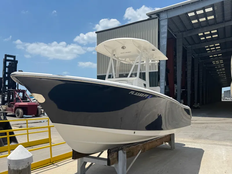 Slide: The Image of 2015 Sea Hunt Ultra 234 boat docked near a large warehouse under a clear blue sky. - 3