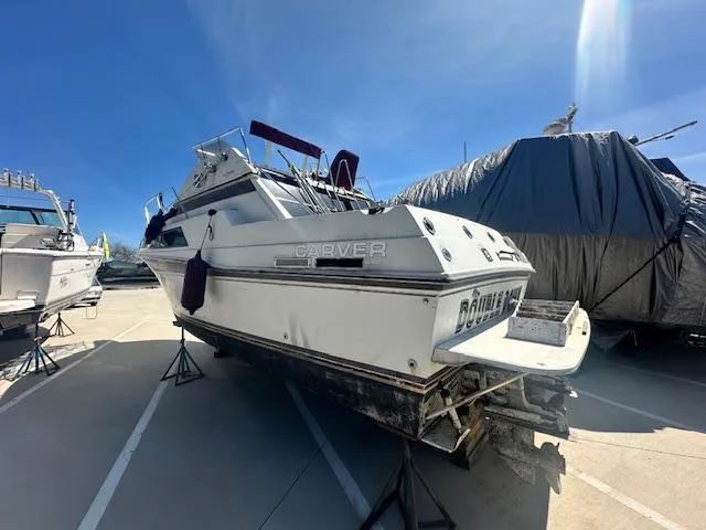 The Image of 1988 Carver 2767 Santego boat on stands, outdoor storage, clear sky background. - 0