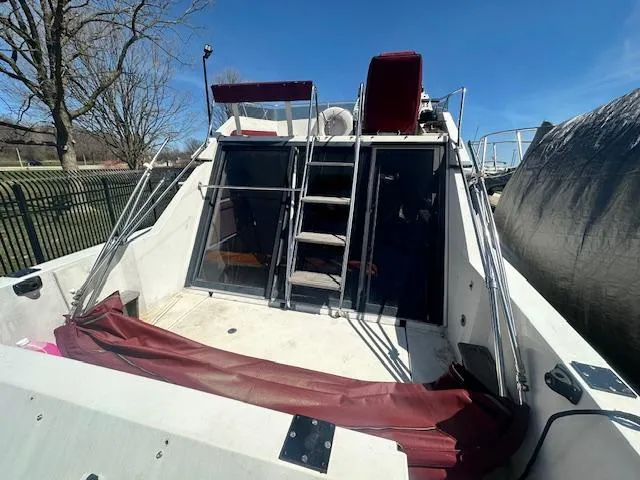 Slide: The Image of 1988 Carver 2767 Santego boat with open deck, ladder, and maroon accents under clear blue sky. - 10