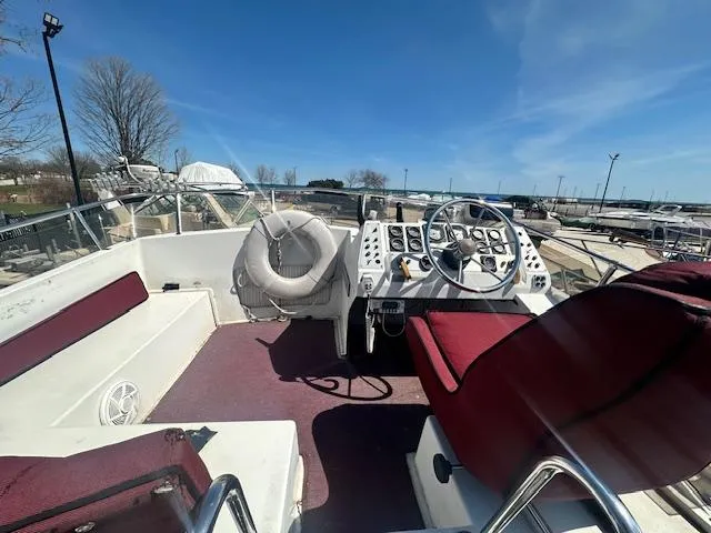 Slide: The Image of 1988 Carver 2767 Santego boat interior with maroon seating and steering wheel, docked outdoors. - 13