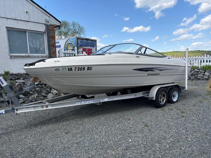 Slide: The Image of 2013 Stingray 208 LR boat on trailer, parked outdoors under a blue sky. - 0