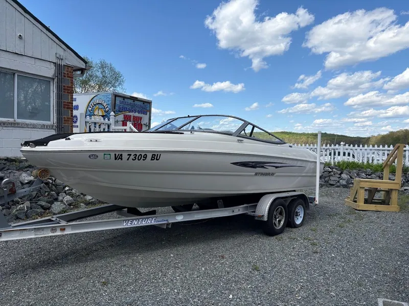 Slide: The Image of 2013 Stingray 208 LR boat on trailer, parked outdoors under a blue sky. - 1