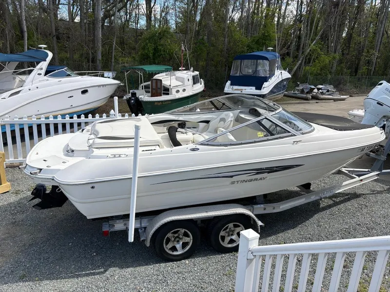Slide: The Image of 2013 Stingray 208 LR boat on trailer, parked in marina with other boats. - 2