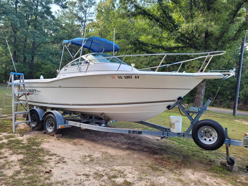 The Image of 1999 Sport-Craft 211 boat on trailer with blue canopy, parked on grassy area. - 0