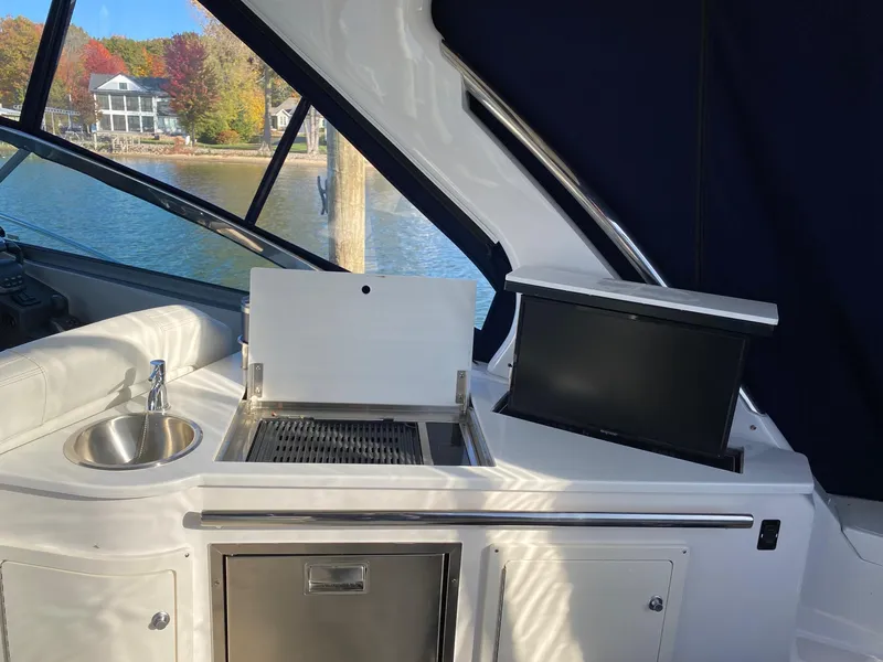 Slide: The Image of 2023 Regal 33 Sport yacht interior with grill and sink, docked by scenic waterfront. - 10