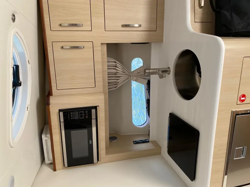 Slide: The Image of 2023 Regal 33 Sport yacht interior with modern kitchenette, featuring wood cabinets and a microwave. - 26