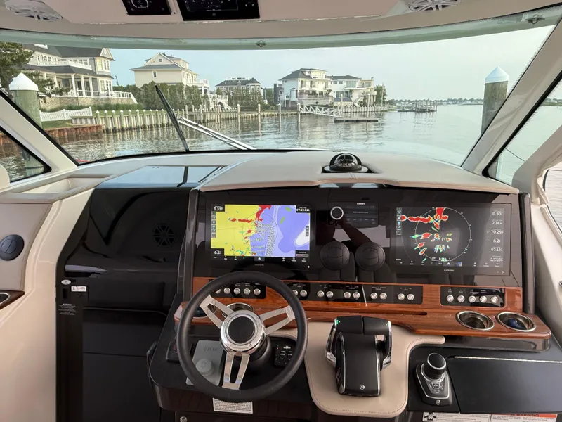 Slide: The Image of 2023 Tiara Yachts 43 LS helm with advanced navigation displays, overlooking waterfront homes. - 34