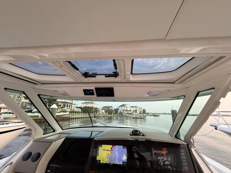 Slide: The Image of 2023 Tiara Yachts 43 LS helm view with navigation screens, overlooking a serene waterfront. - 35