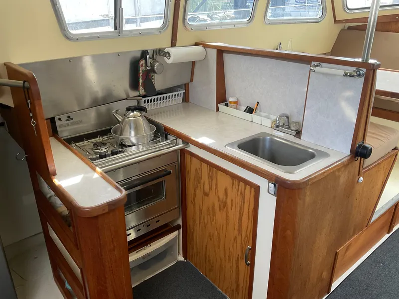 Slide: The Image of 1980 Kanter Staysail Cutter galley with stove, sink, and wooden cabinetry. - 14