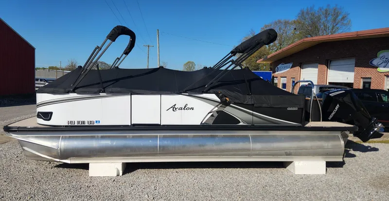 Slide: The Image of 2024 Avalon LSZ 2385 Rear Lounger pontoon boat with black cover, parked outdoors. - 13