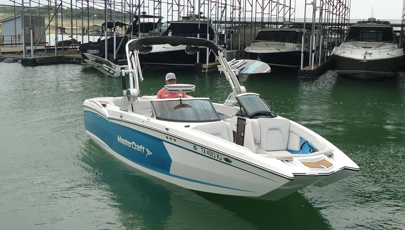 Slide: The Image of 2021 MasterCraft XStar boat in marina, featuring sleek design and blue accents. - 0