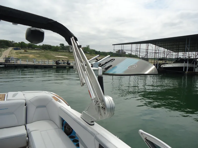 Slide: The Image of 2021 MasterCraft XStar boat docked on a calm lake near a marina. - 16