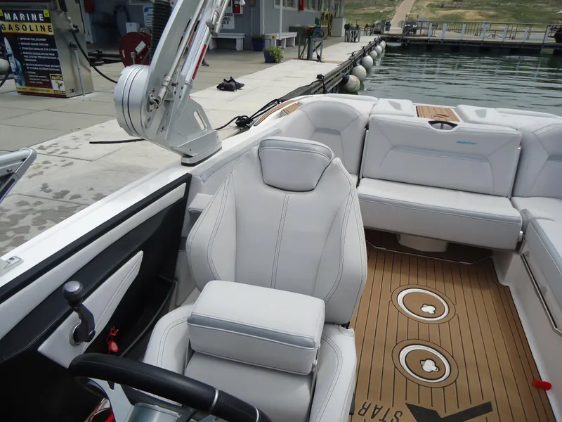 Slide: The Image of 2021 MasterCraft XStar boat interior with white seating and wooden flooring at a dock. - 18