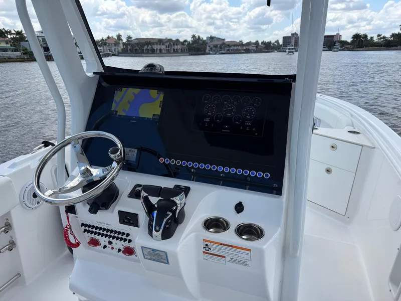 Slide: The Image of 2023 Edgewater 262CC boat dashboard with steering wheel and navigation display on a calm waterway. - 11