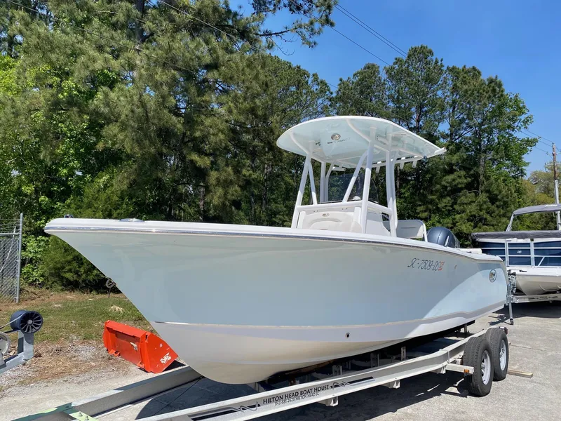 Slide: The Image of 2022 Sea Hunt Ultra 229 boat on trailer, surrounded by trees and clear blue sky. - 1