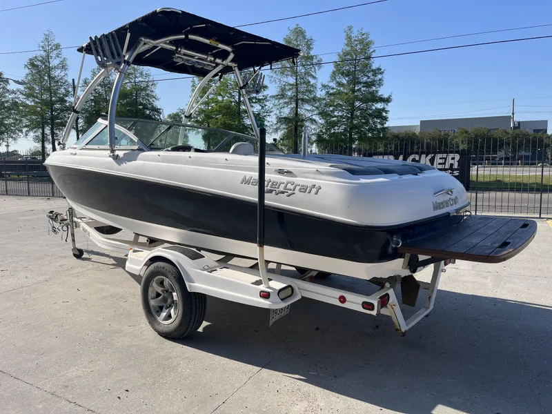 Slide: The Image of 2006 MasterCraft MariStar 210 boat on trailer, black and white, with canopy, parked outdoors. - 2