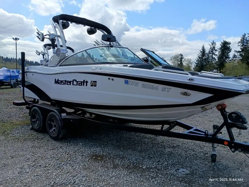 Slide: The Image of 2021 MasterCraft XT20 boat on trailer, parked outdoors under cloudy sky. - 2