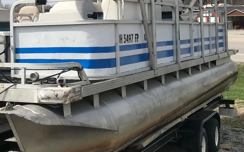 Slide: The Image of 1995 Manitou 24 Spirit pontoon boat on trailer, featuring blue stripes and visible registration number. - 7