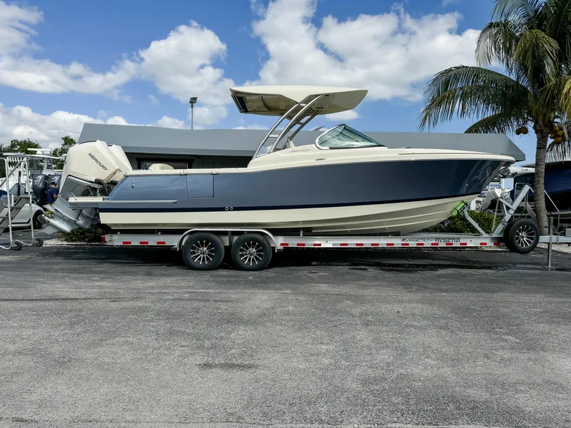 The Image of 2025 Chris-Craft Calypso 28 boat on trailer, parked outdoors under blue sky. - 0
