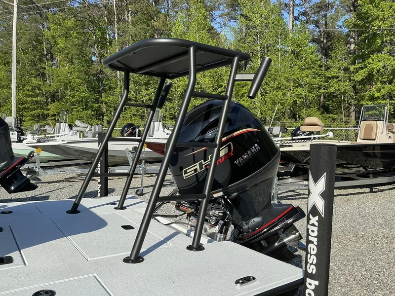 Slide: The Image of 2025 Xpress Skiff 185 with Yamaha engine, parked outdoors, surrounded by trees and other boats. - 10