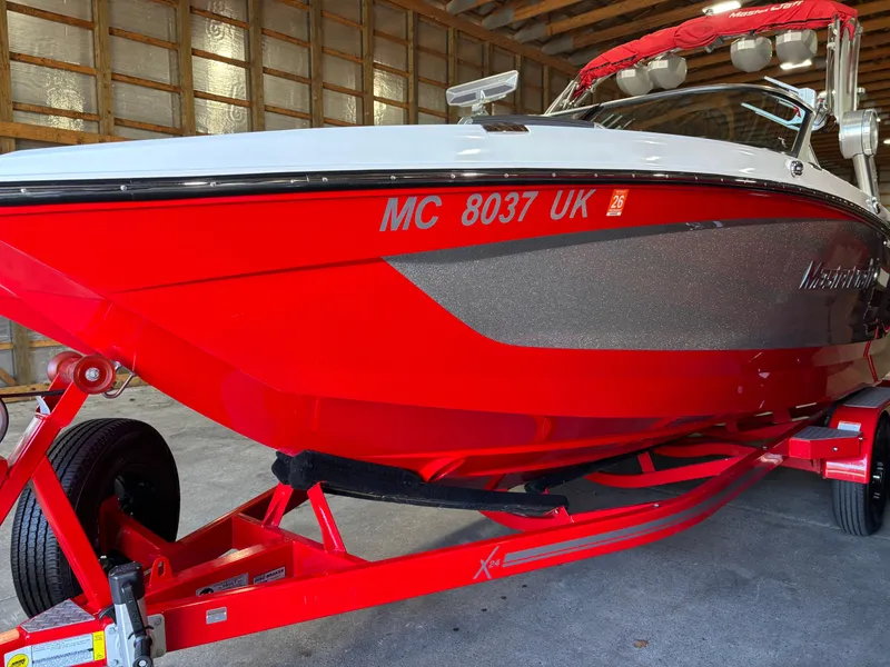 Slide: The Image of 2020 MasterCraft X24 boat in vibrant red, parked indoors on a matching trailer. - 21