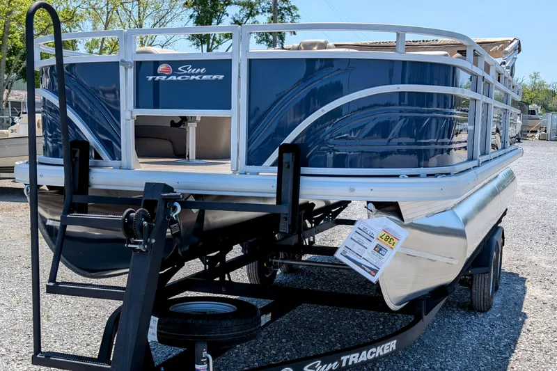 Slide: The Image of 2025 Sun Tracker Fishin' Barge 20 DLX pontoon boat on trailer, parked outdoors. - 2