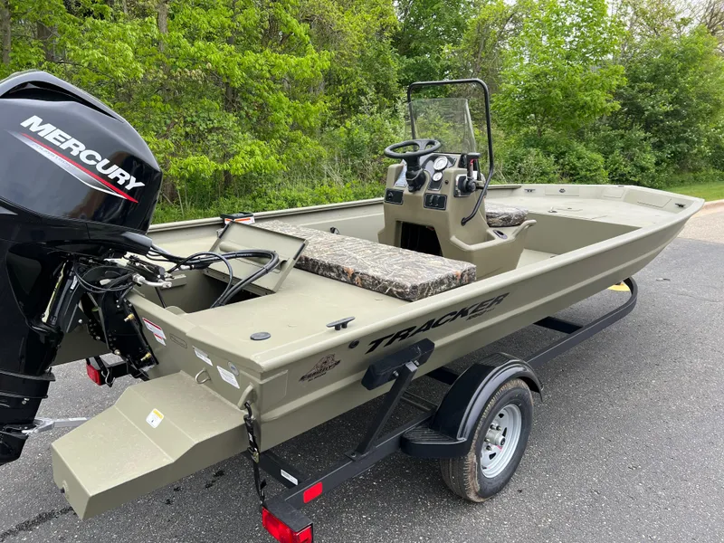 Slide: The Image of 2025 Tracker Grizzly 1860 CC boat with Mercury engine on trailer, parked outdoors. - 2