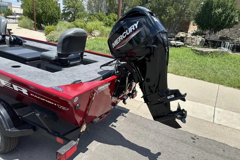 Slide: The Image of 2025 Tracker Panfish 17 boat with Mercury outboard motor, parked on a sunny street. - 2