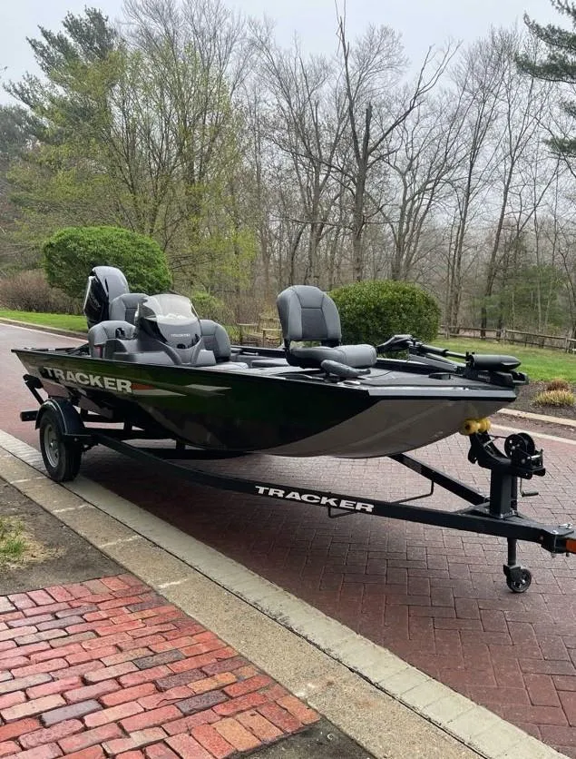 Slide: The Image of 2025 Tracker Pro 170 boat on trailer, parked on brick road, surrounded by trees. - 2