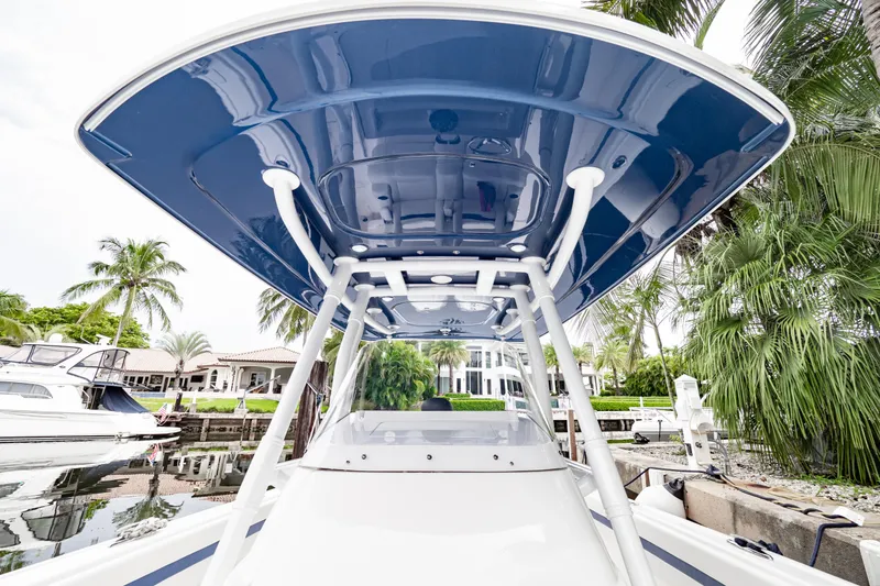Slide: The Image of 2018 Intrepid 327 Center Console boat with blue canopy, docked near palm trees. - 17