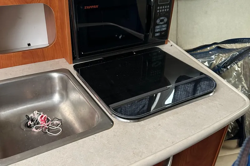 Slide: The Image of 2005 Bayliner 245 CIERA kitchenette with sink, stove, and microwave. - 11